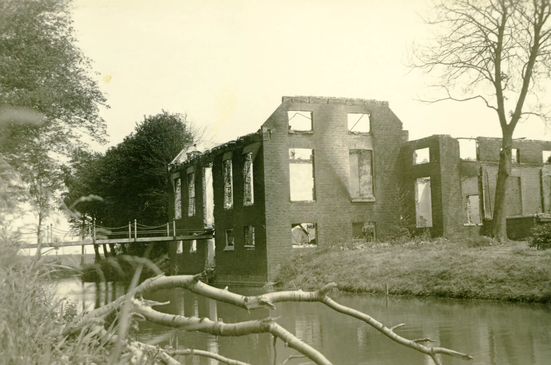Verwoeste boerderij aan het water met een loopbrug naar het gebouw. 