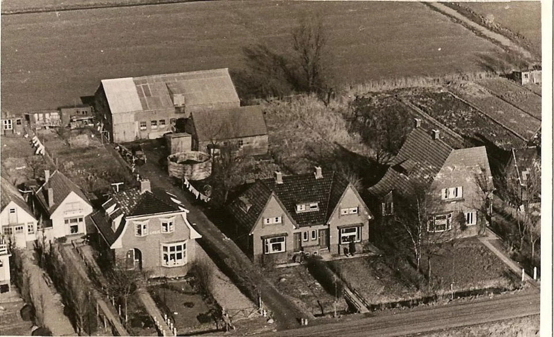 Luchtfoto van de boerderij en de schuren van Anna Vos aan de rand van een veld.