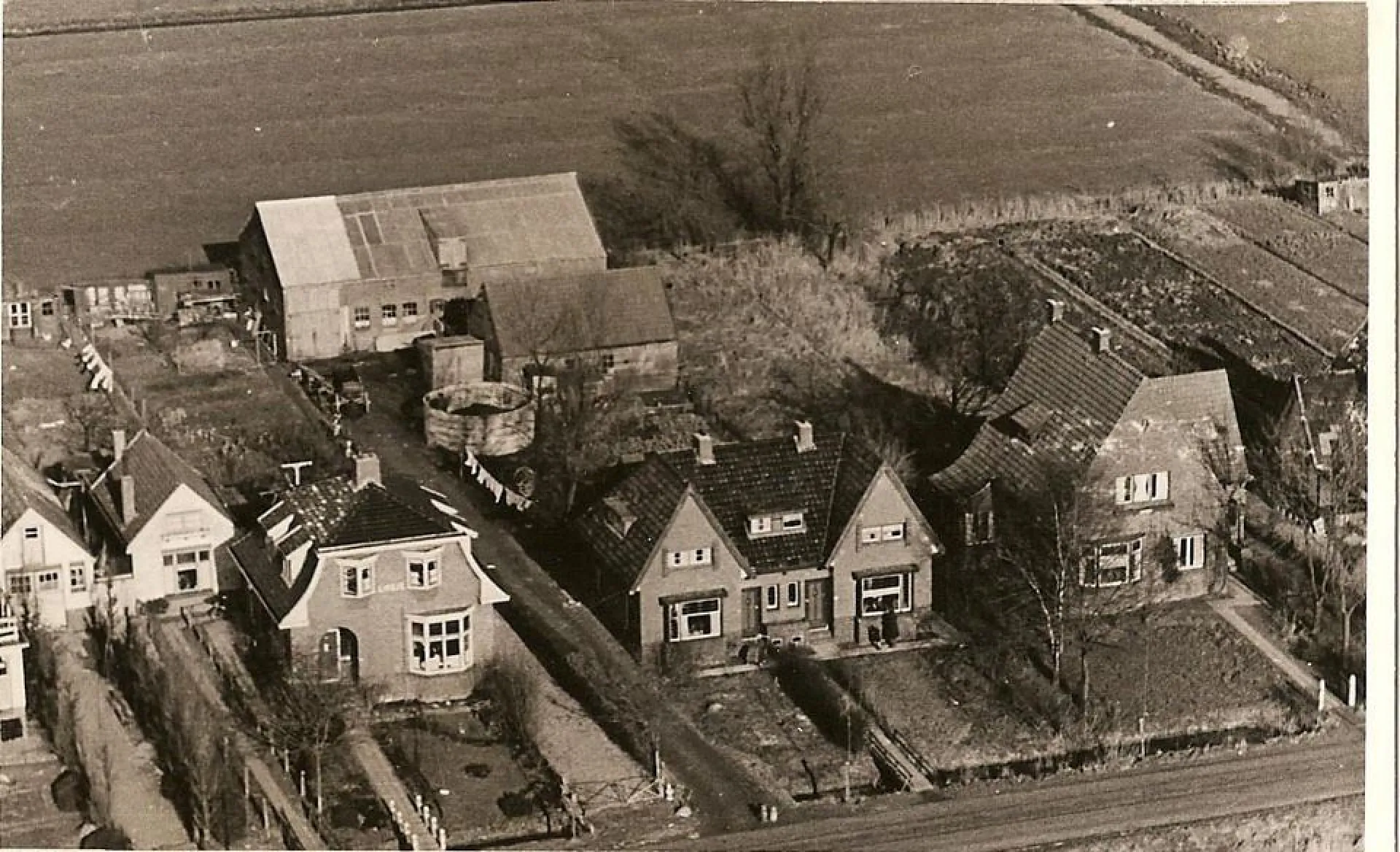 Luchtfoto van de boerderij en de schuren van Anna Vos aan de rand van een veld.