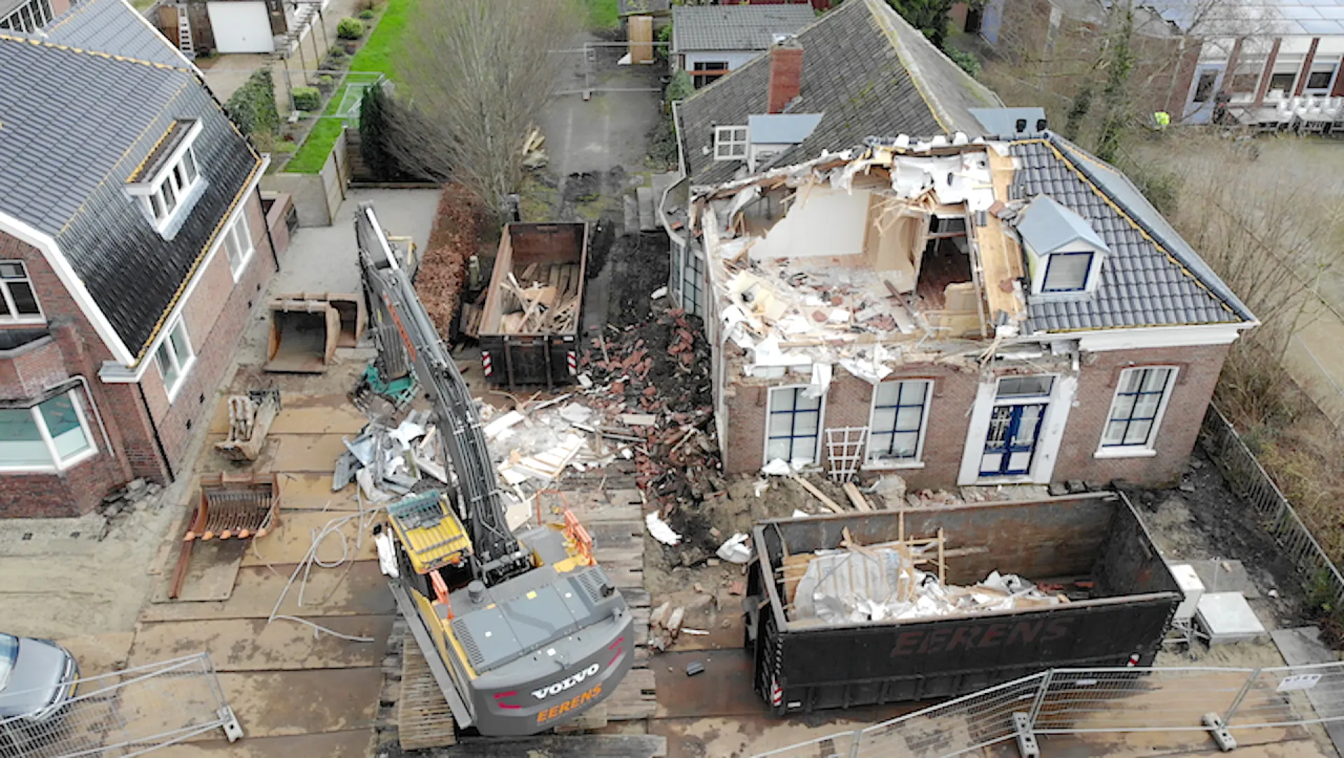 Een woning in Overschild wordt gesloopt met een bouwmachine en er staat een puincontainer.