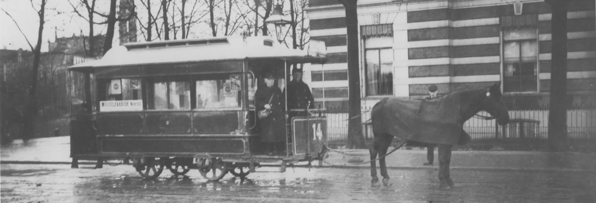 Paardentram stopt voor een groot gebouw op een regenachtige dag.