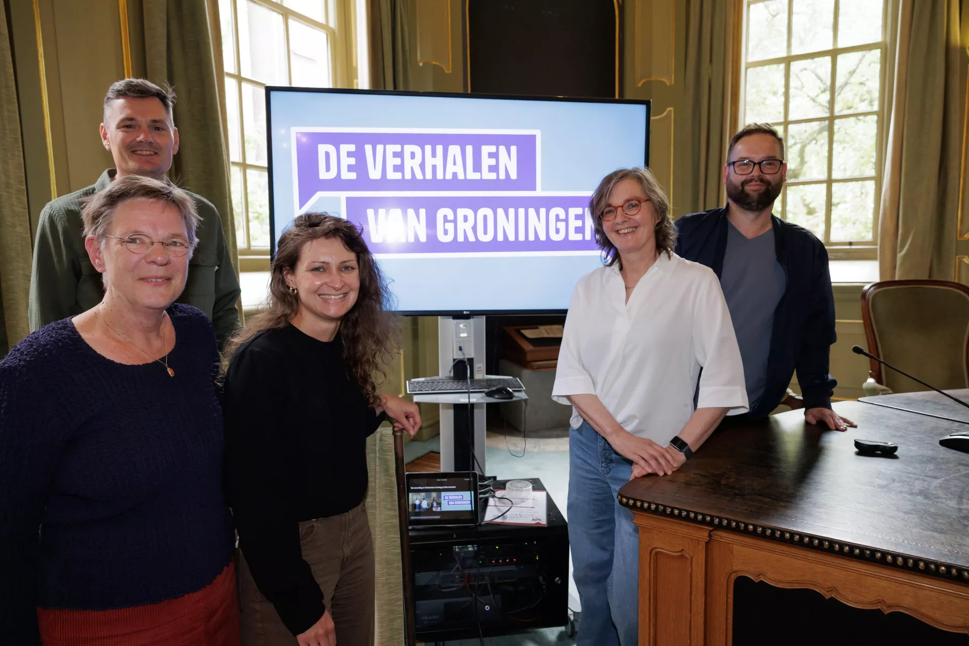 Een groep mensen poseert bij een scherm met de tekst "De Verhalen van Groningen".