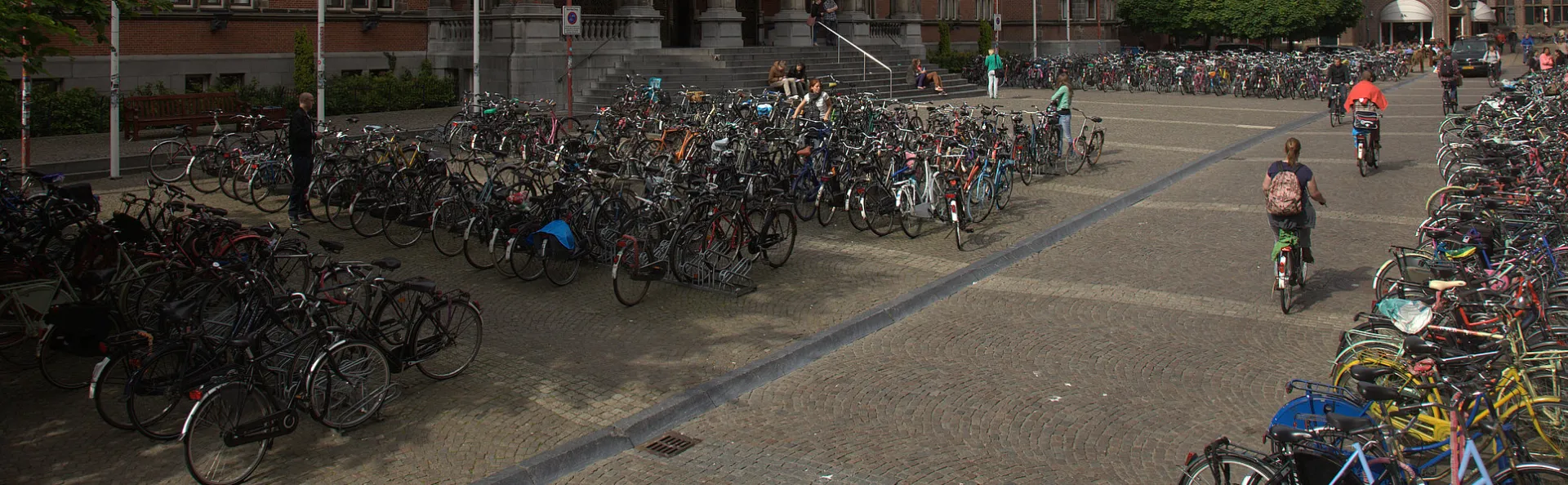 Fietsen geparkeerd op het Broersplein bij het Academiegebouw van de Rijksuniversiteit Groningen, met mensen die fietsen.