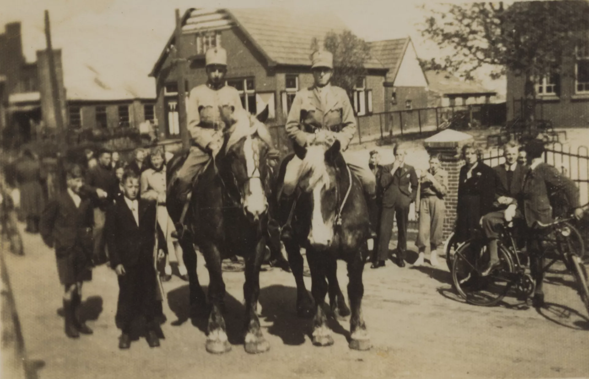 Twee soldaten te paard omringd door mensen in een dorpsstraat.