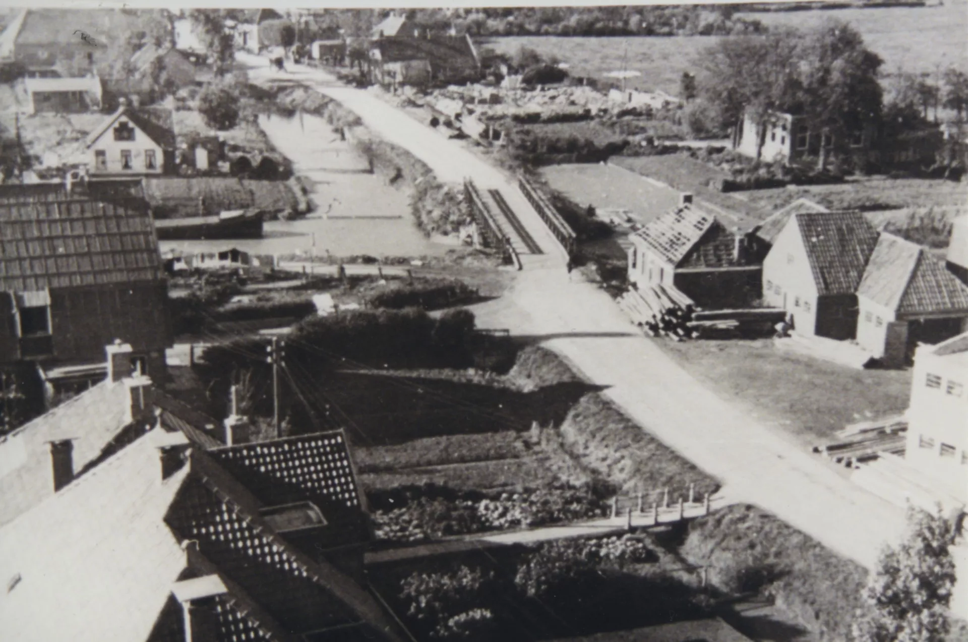 Luchtfoto van een dorp met beschadigde huizen en een noodbrug over het kanaal met daarachter de restanten van een kapotgeschoten hotel.