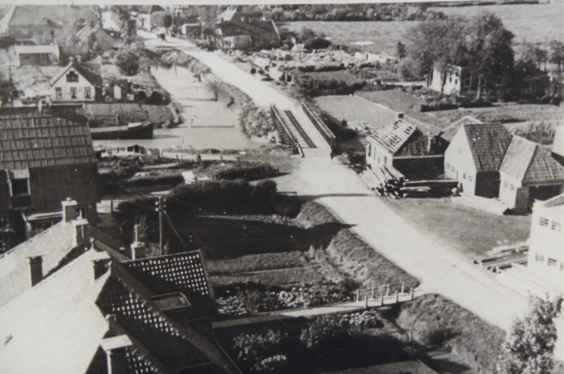 Luchtfoto van een dorp met beschadigde huizen en een noodbrug over het kanaal met daarachter de restanten van een kapotgeschoten hotel.
