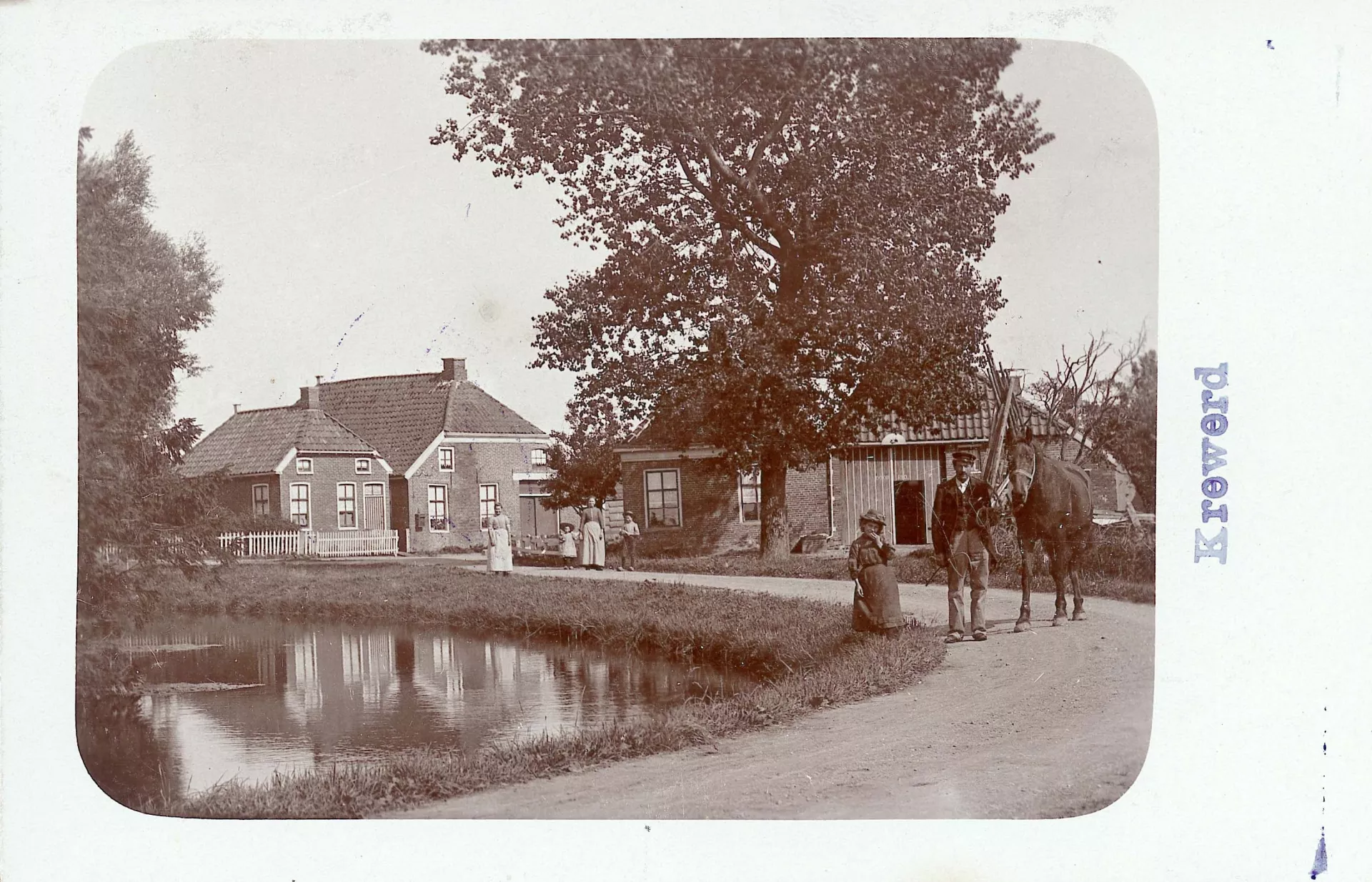Fotokaart met dorpsgezicht. Een rustiek dorps tafereel met mensen en huizen langs een waterkant.