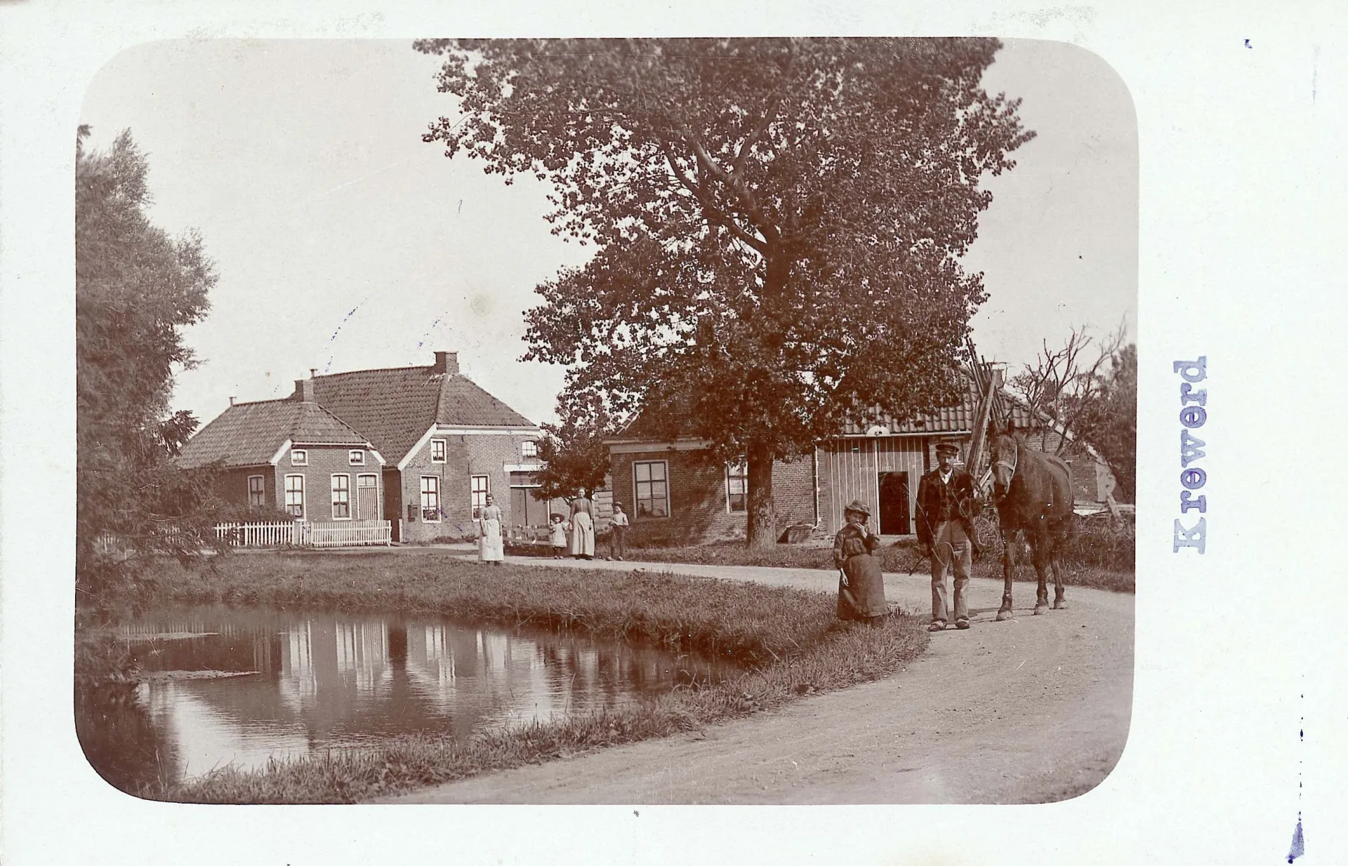 Fotokaart met dorpsgezicht. Een rustiek dorps tafereel met mensen en huizen langs een waterkant.