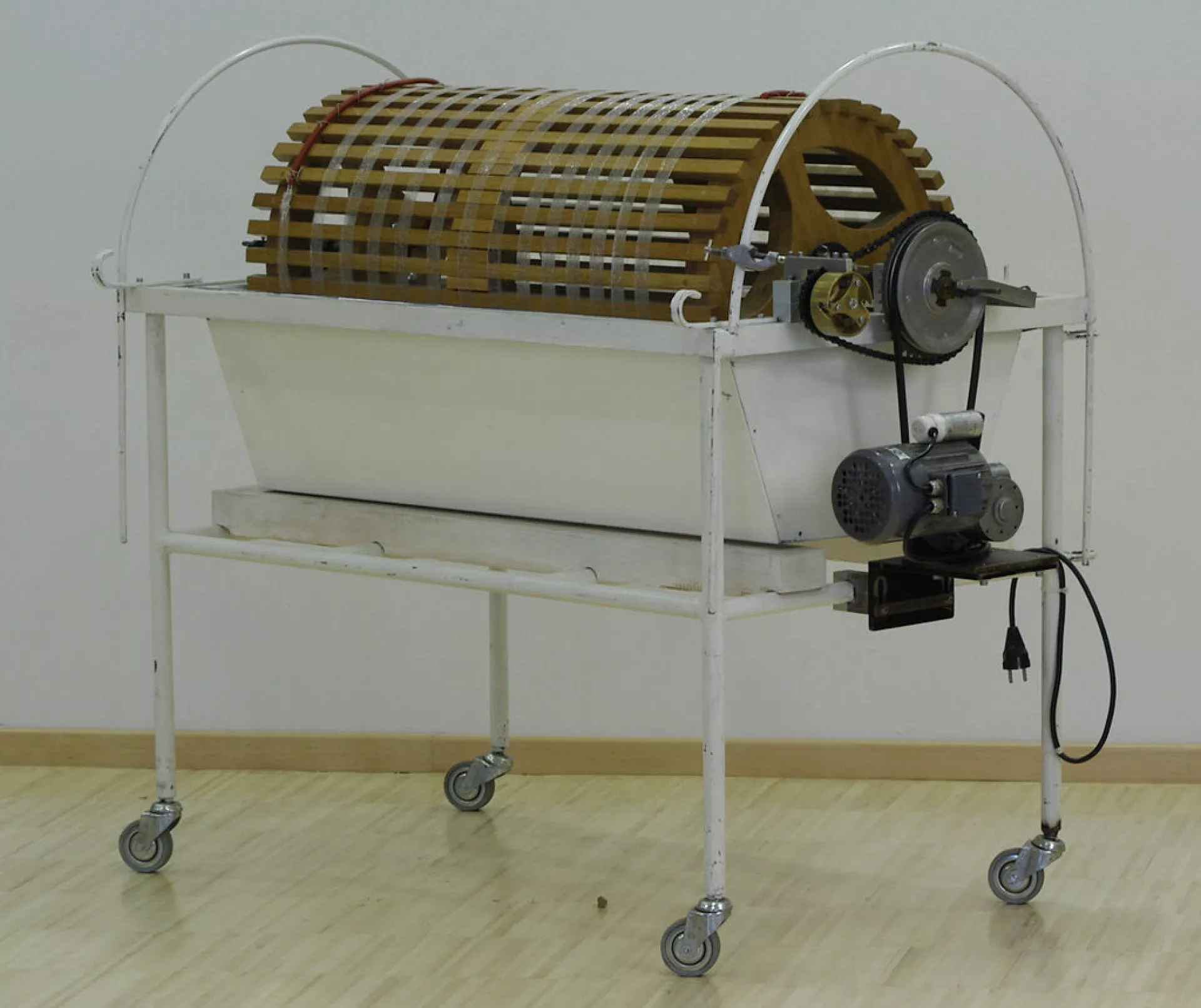 Een kunstmatige nier bestaande uit een wit metalen bak op een rek met wieltjes, met een houten trommel en elektrische aandrijving.