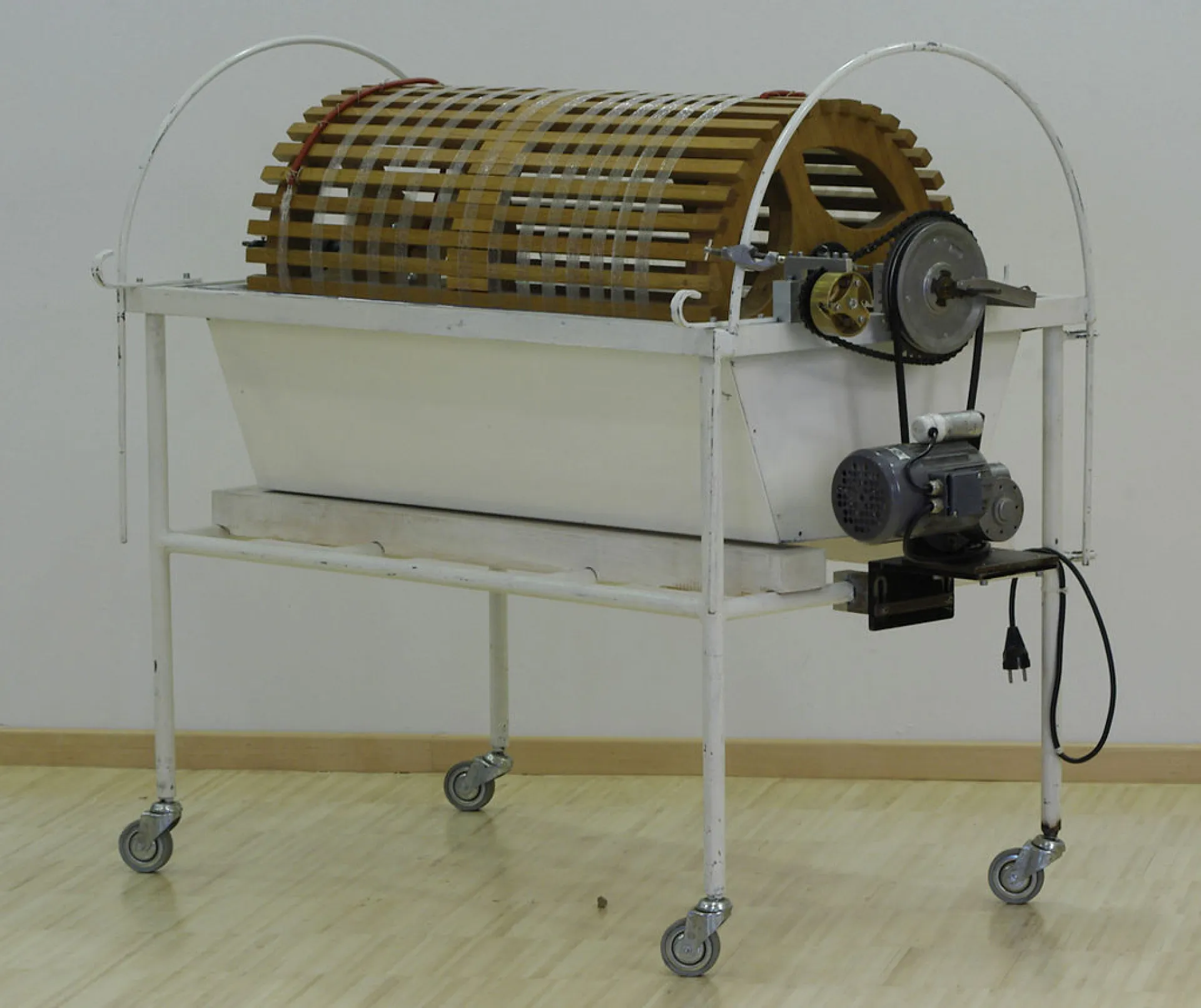 Een kunstmatige nier bestaande uit een wit metalen bak op een rek met wieltjes, met een houten trommel en elektrische aandrijving.