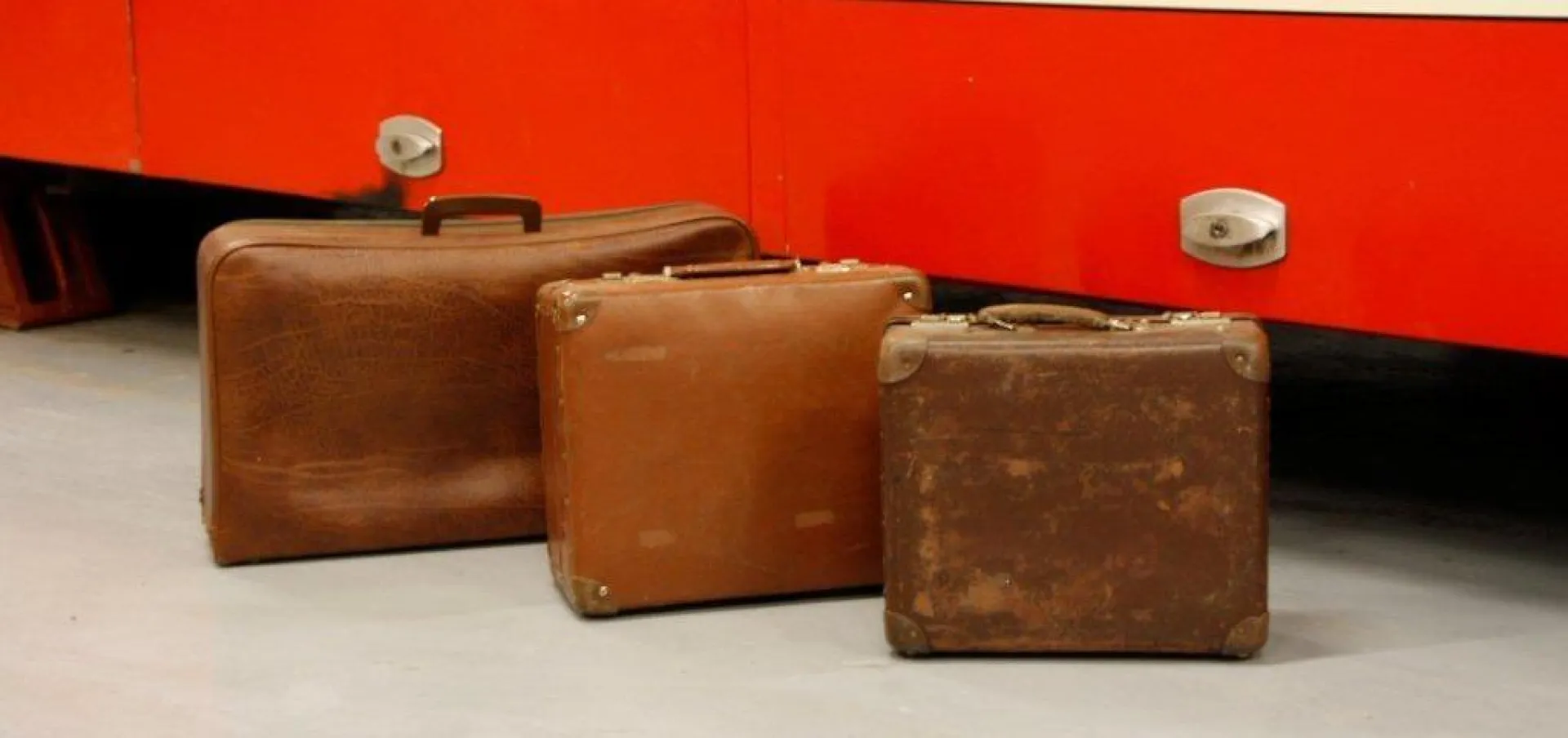 Drie bruine vintage koffers voor een rode achtergrond.