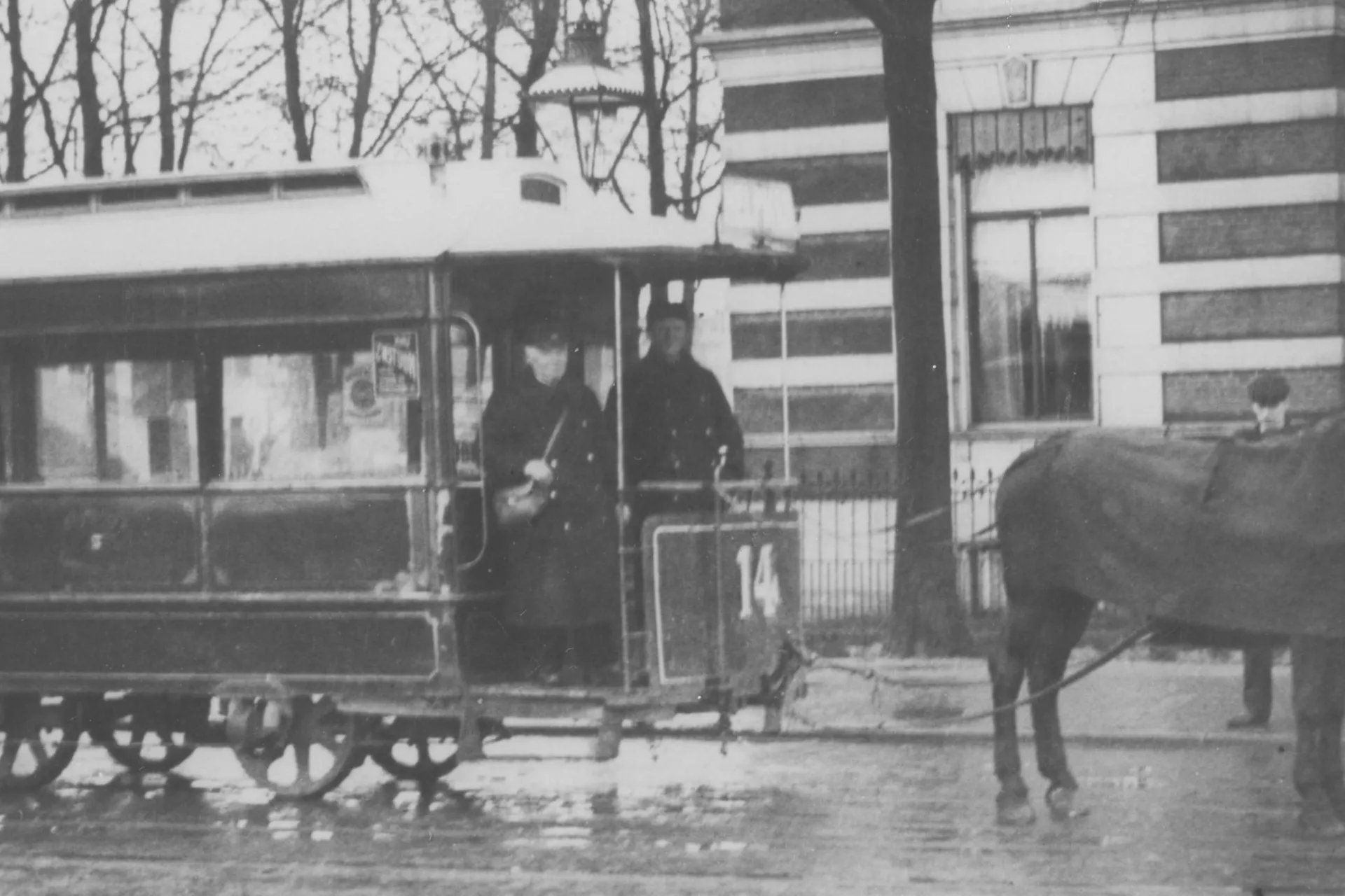 Paardentram stopt voor een groot gebouw op een regenachtige dag.
