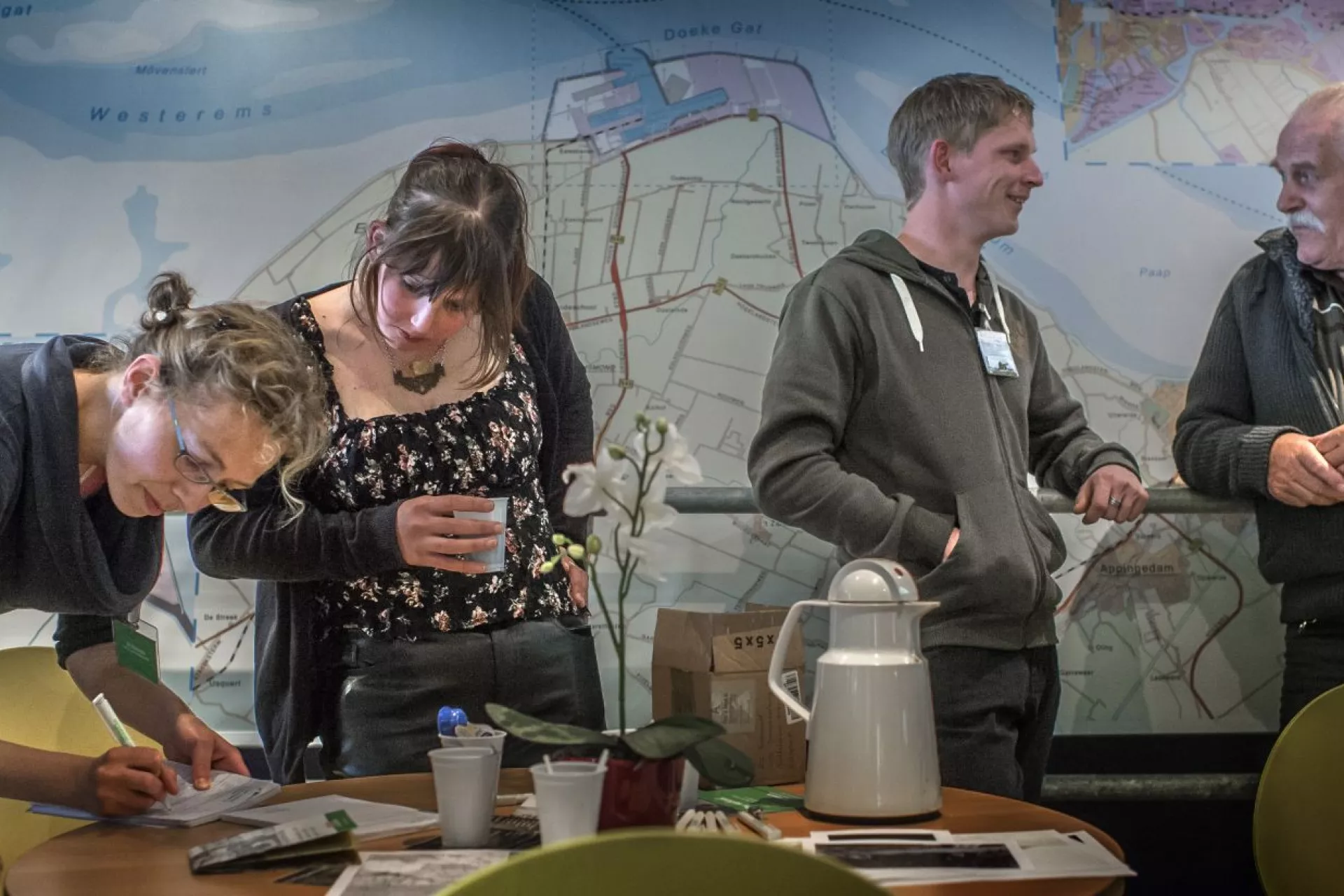 Een groep mensen in gesprek rond een tafel, met een kaart op de muur.