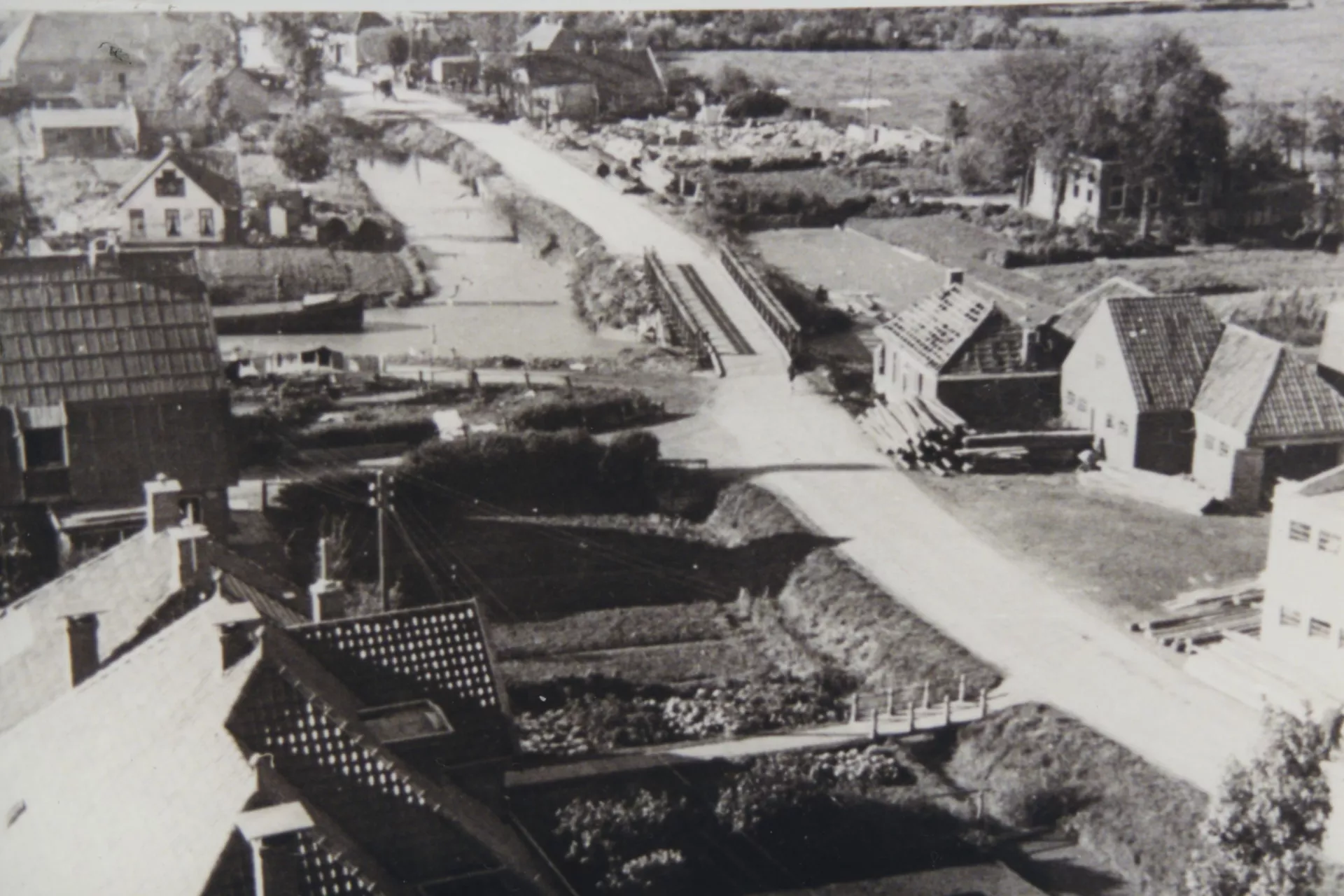 Luchtfoto van een dorp met beschadigde huizen en een noodbrug over het kanaal met daarachter de restanten van een kapotgeschoten hotel.