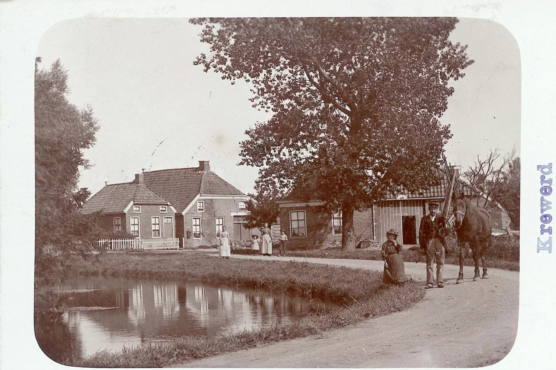 Fotokaart met dorpsgezicht. Een rustiek dorps tafereel met mensen en huizen langs een waterkant.