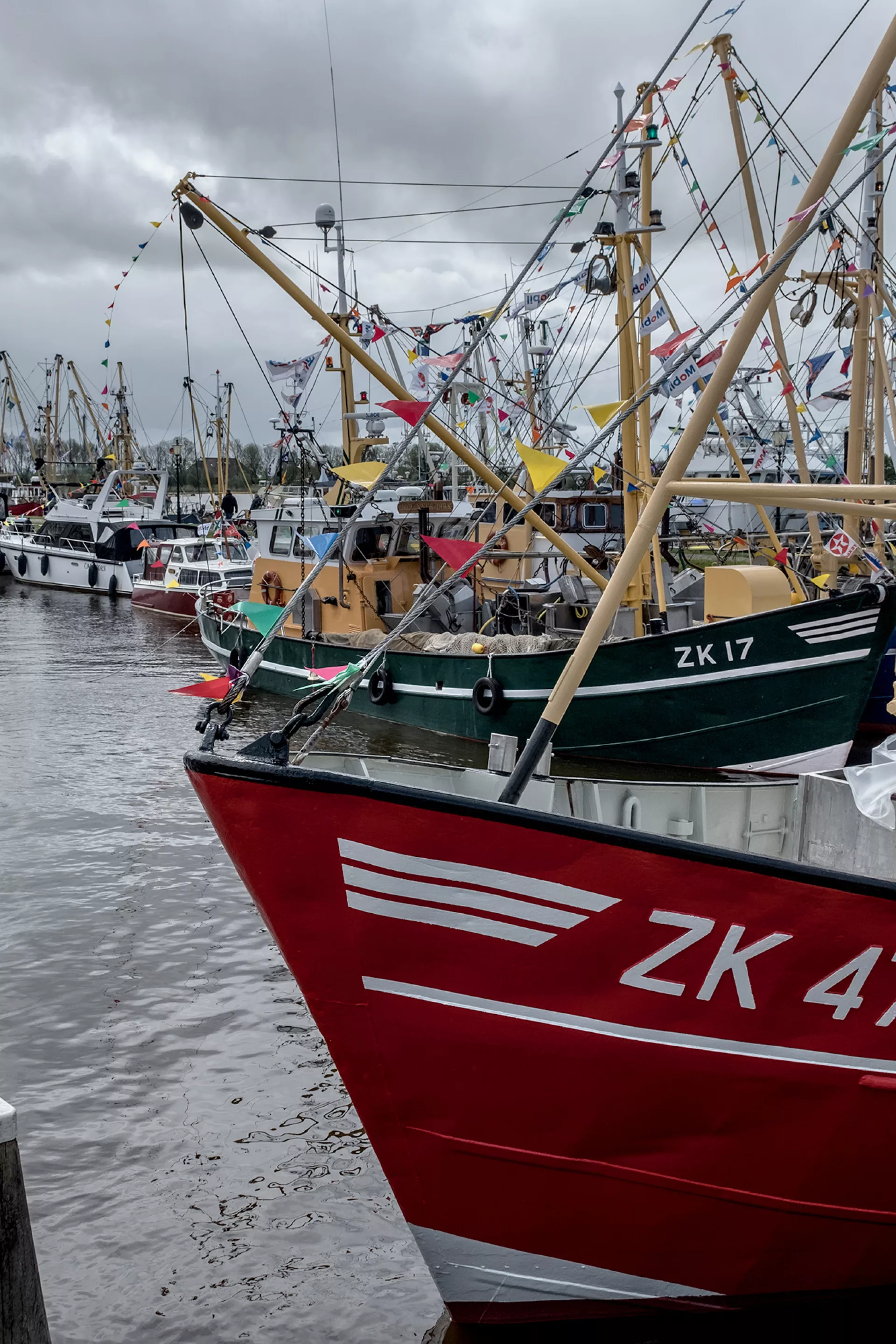 Vissersboten aangemeerd in een drukke haven onder een bewolkte hemel.