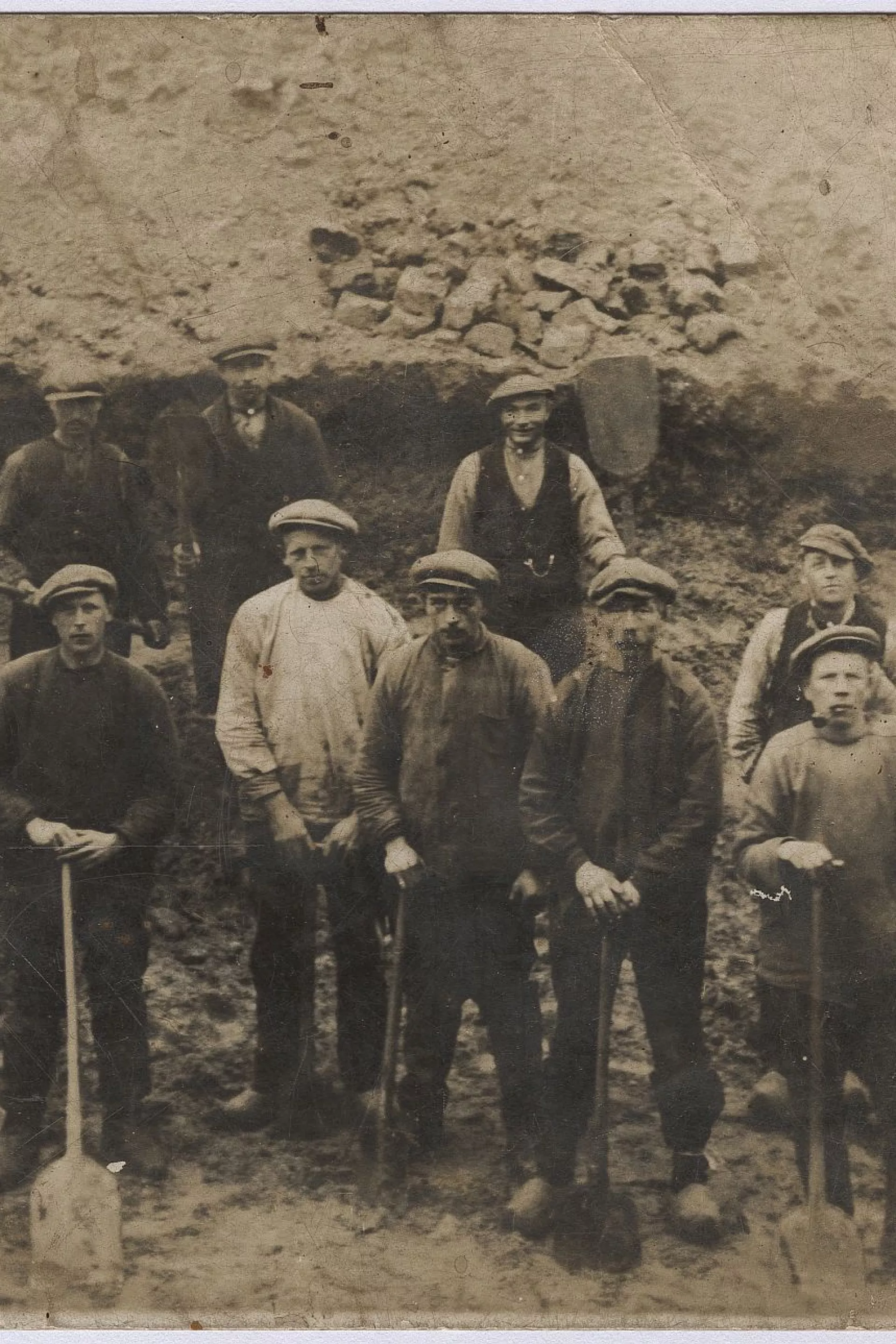 Een groep mannen poseert met scheppen in een gegraven kanaal.