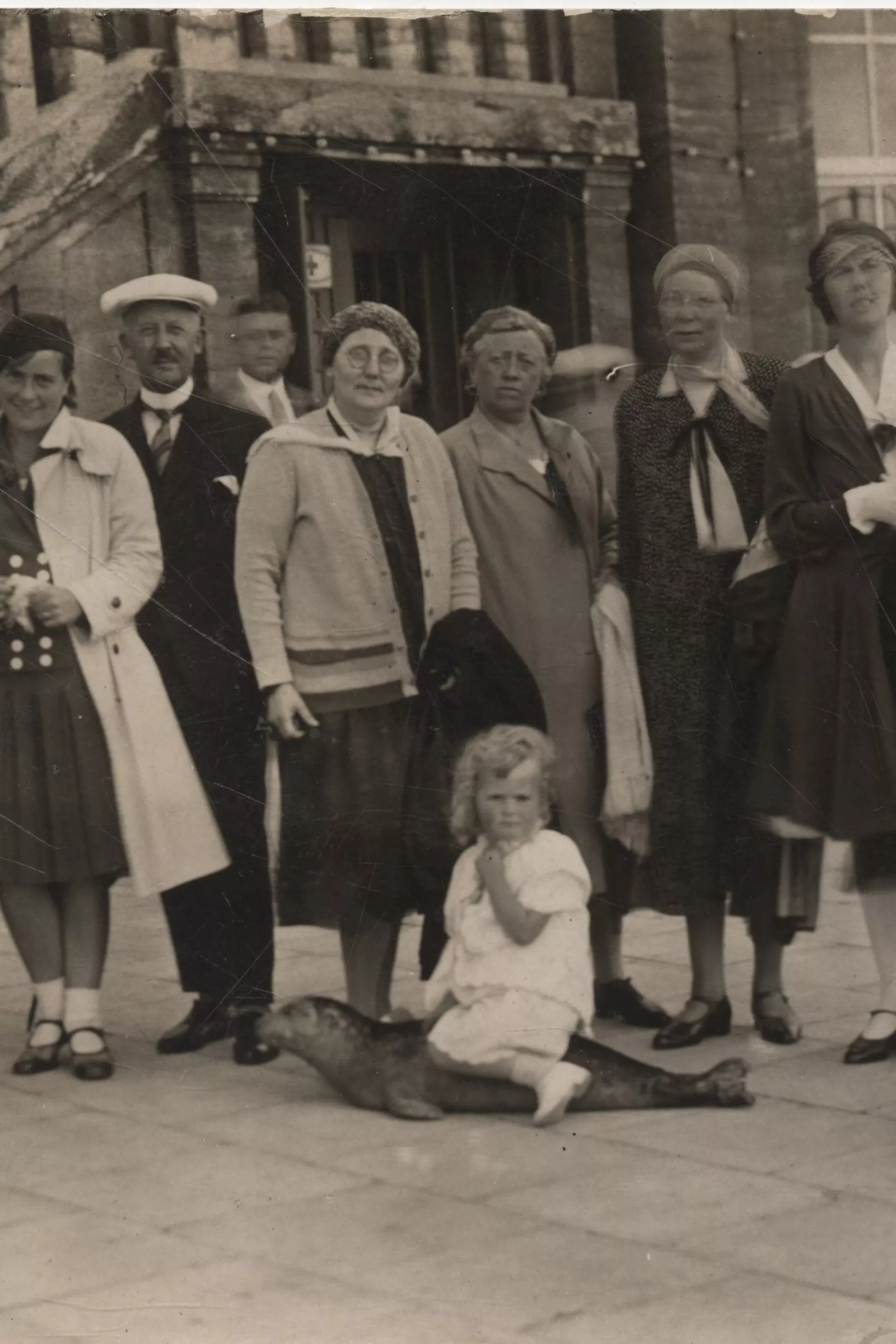 Een groep vrouwen poseert staand voor een foto op een plein, met een kindje zittend op een zeehondje ervoor.